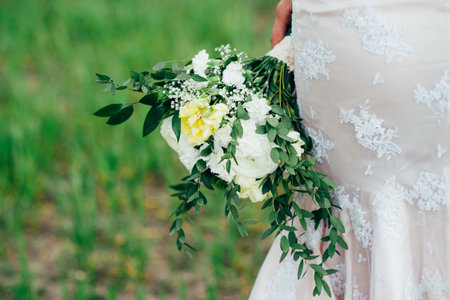 bride with a bouquet in an ivory dress and a knitted shawl on a green fieldの写真素材