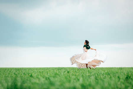 bride with a bouquet in an ivory dress and a knitted shawl on a green fieldの写真素材
