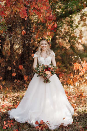 blonde girl in a wedding dress in the autumn forest against the background of wild red grapesの写真素材