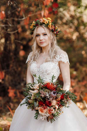 blonde girl in a wedding dress in the autumn forest against the background of wild red grapesの写真素材