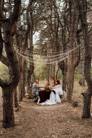 wedding dinner of a newlywed couple in the autumn forest on the background of the wedding ceremony areaの写真素材