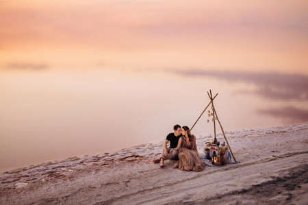 young couple having a picnic on the beach of a pink lake