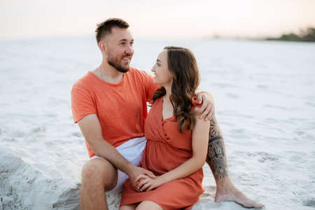 young couple in orange clothes with dog in the desert white sandsの写真素材