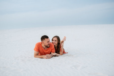 young couple in orange clothes with dog in the desert white sandsの写真素材