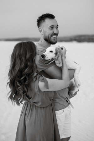 young couple in orange clothes with dog in the desert white sandsの写真素材