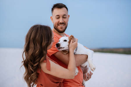 young couple in orange clothes with dog in the desert white sandsの写真素材