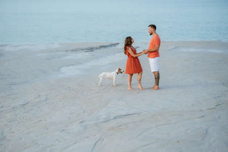 young couple in orange clothes with dog on an empty sandy beachの写真素材