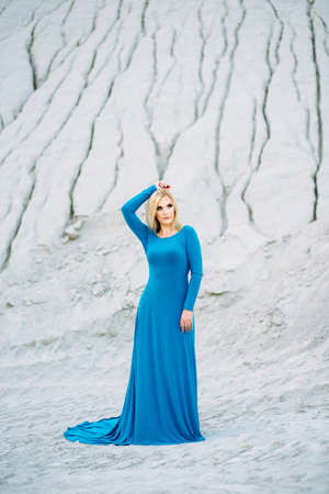 blonde girl in a blue dress with blue eyes in a granite quarry against the background of gravelの写真素材