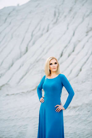 blonde girl in a blue dress with blue eyes in a granite quarry against the background of gravelの写真素材