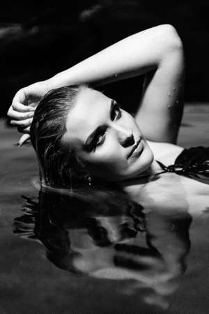 blonde girl in a black dress with blue eyes on the stone coast of the riverの写真素材