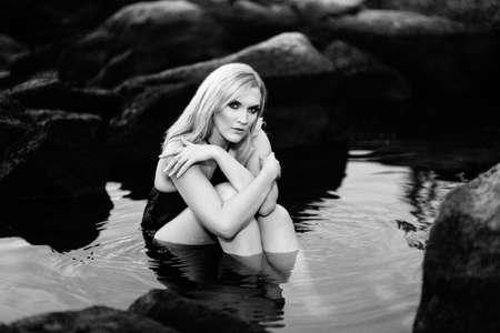 blonde girl in a black dress with blue eyes on the stone coast of the riverの写真素材