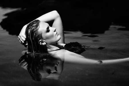 blonde girl in a black dress with blue eyes on the stone coast of the riverの写真素材