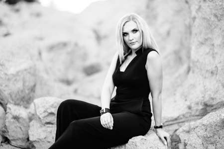 blonde girl in a black trouser suit with blue eyes on the background of a granite quarry from gray...
