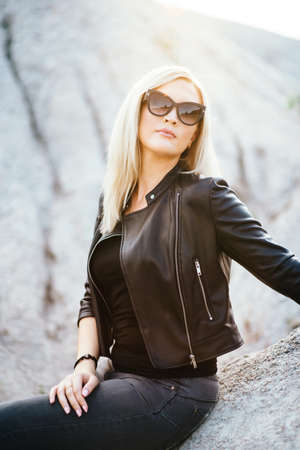 blonde girl in a black trouser suit with blue eyes on the background of a granite quarry from gray rubbleの写真素材