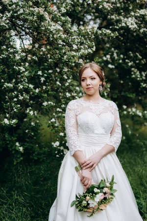 bride with a wedding bouquet in the forest near the bushes blooming with white flowersの写真素材
