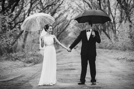 bride and groom on a rainy wedding day walking under an umbrellaの写真素材