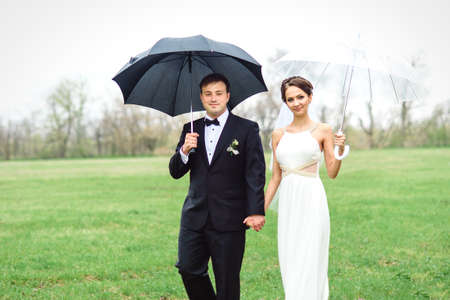 bride and groom on a rainy wedding day walking under an umbrellaの写真素材