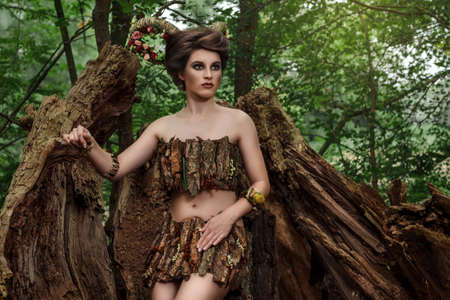 girl with braided horns in a dress made of bark on a forest path near the fallen treesの写真素材