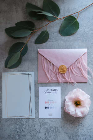 wedding invitation in a gray envelope on a table with green sprigs