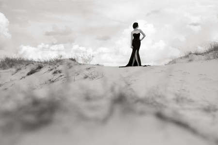 girl in a black long dress in a sandy desert under a blue skyの写真素材
