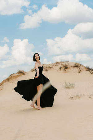 girl in a black long dress in a sandy desert under a blue skyの写真素材