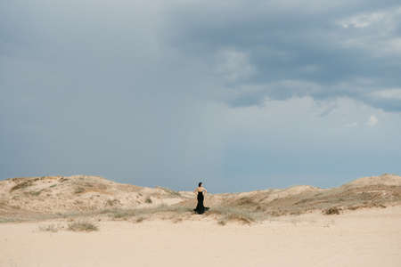 girl in a black long dress in a sandy desert under a blue skyの写真素材