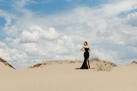 girl in a black long dress in a sandy desert under a blue skyの写真素材