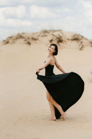 girl in a black long dress in a sandy desert under a blue skyの写真素材