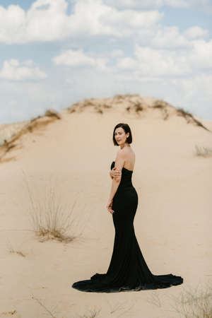 girl in a black long dress in a sandy desert under a blue skyの写真素材