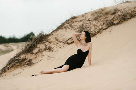 girl in a black long dress in a sandy desert under a blue skyの写真素材