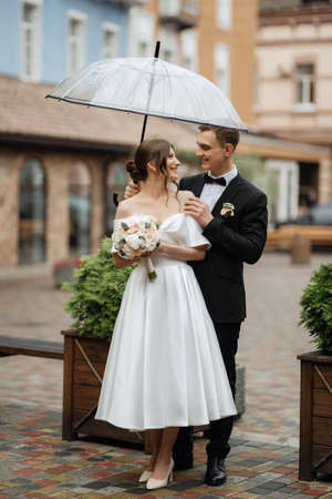 young couple bride and groom in a white short dress walking in the rainの写真素材