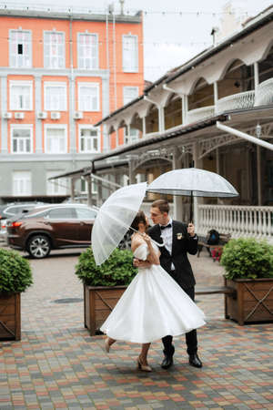 young couple bride and groom in a white short dress walking in the rainの写真素材