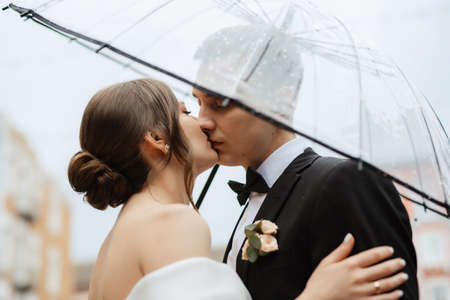 young couple bride and groom in a white short dress walking in the rainの写真素材