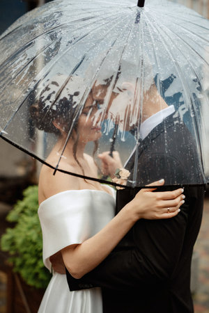 young couple bride and groom in a white short dress walking in the rainの写真素材