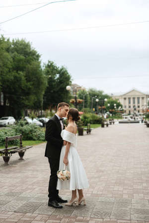 young couple bride and groom in a white short dress walking in the rainの写真素材