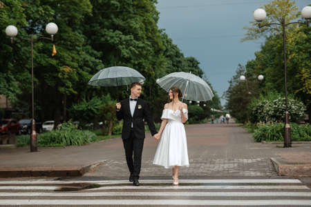 young couple bride and groom in a white short dress walking in the rainの写真素材