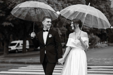 young couple bride and groom in a white short dress walking in the rainの写真素材