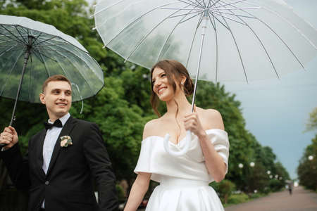 young couple bride and groom in a white short dress walking in the rainの写真素材
