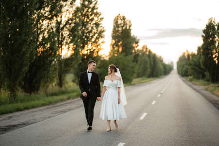 young couple bride and groom in a white short dress walking in the rainの写真素材