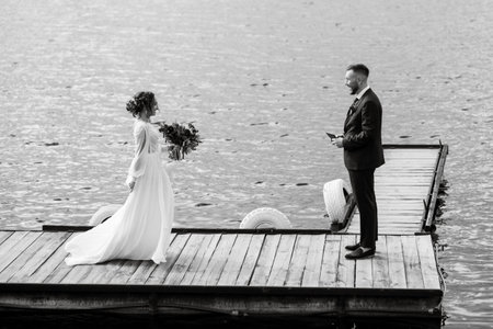 the first meeting of the bride and groom in wedding dresses on the pier near the waterの写真素材
