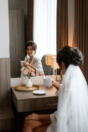 bride in a veil with makeup drinks morning coffee in a hotelの写真素材