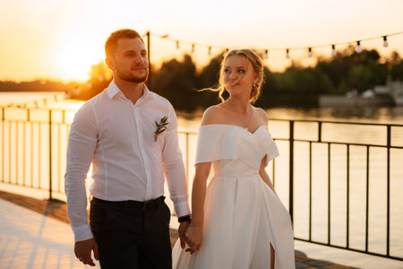 bride and groom against the backdrop of a yellow sunset on a pier near the riverの写真素材