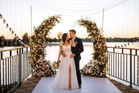 bride and groom against the backdrop of a yellow sunset on a pier near the riverの写真素材