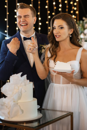 newlyweds happily cut, laugh and taste the wedding cakeの写真素材