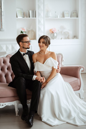 groom in a black suit with a bow tie and the bride in a tight white dress in a bright studioの写真素材