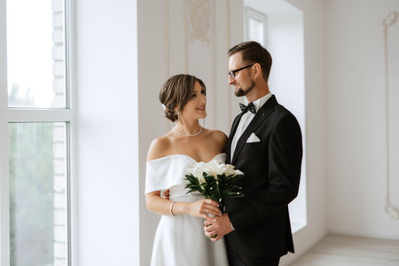 groom in a black suit with a bow tie and the bride in a tight white dress in a bright studioの写真素材