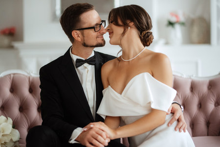 groom in a black suit with a bow tie and the bride in a tight white dress in a bright studioの写真素材