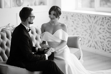 groom in a black suit with a bow tie and the bride in a tight white dress in a bright studioの写真素材