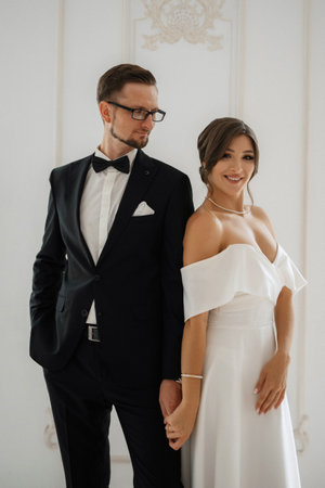 groom in a black suit with a bow tie and the bride in a tight white dress in a bright studioの写真素材