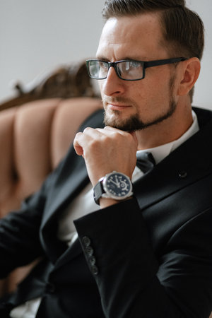 portrait of a groom in a black suit and glasses in a studio in an armchairの写真素材